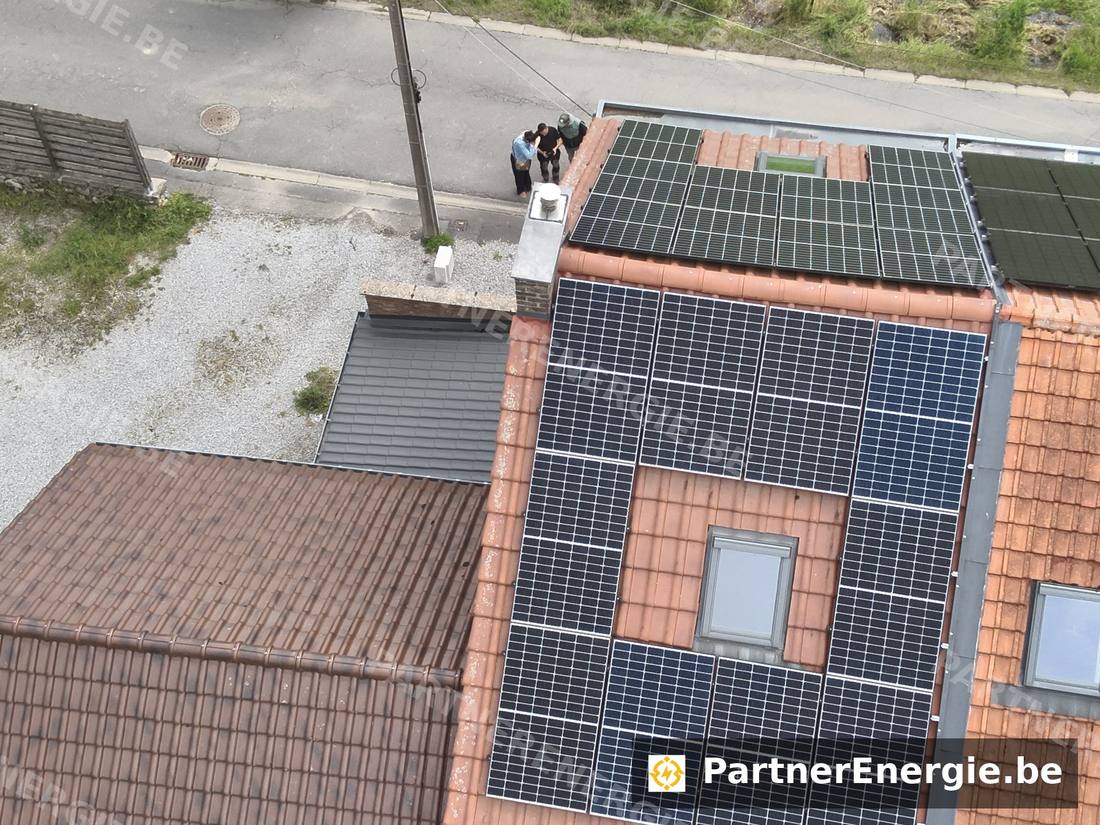 Vue aérienne d'une toiture photovoltaïque avec technicien et clients au sol lors d'une inspection drone