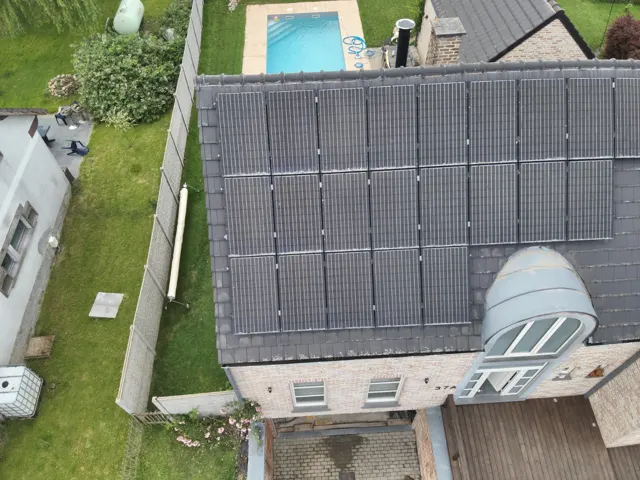 Télépilote préparant un drone thermique devant une maison équipée de panneaux solaires